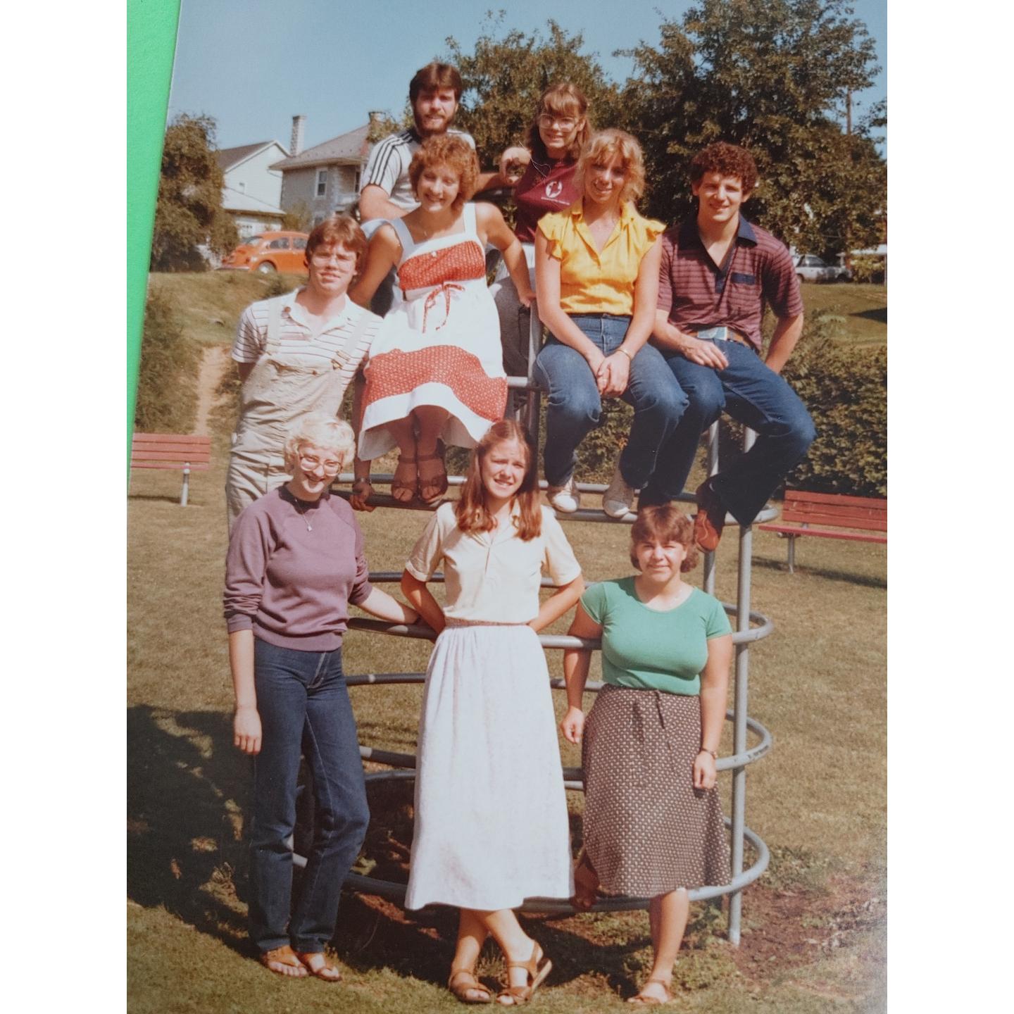 A group of 9 people pose for the camera on a jungle gym. This photo is from the 1980s