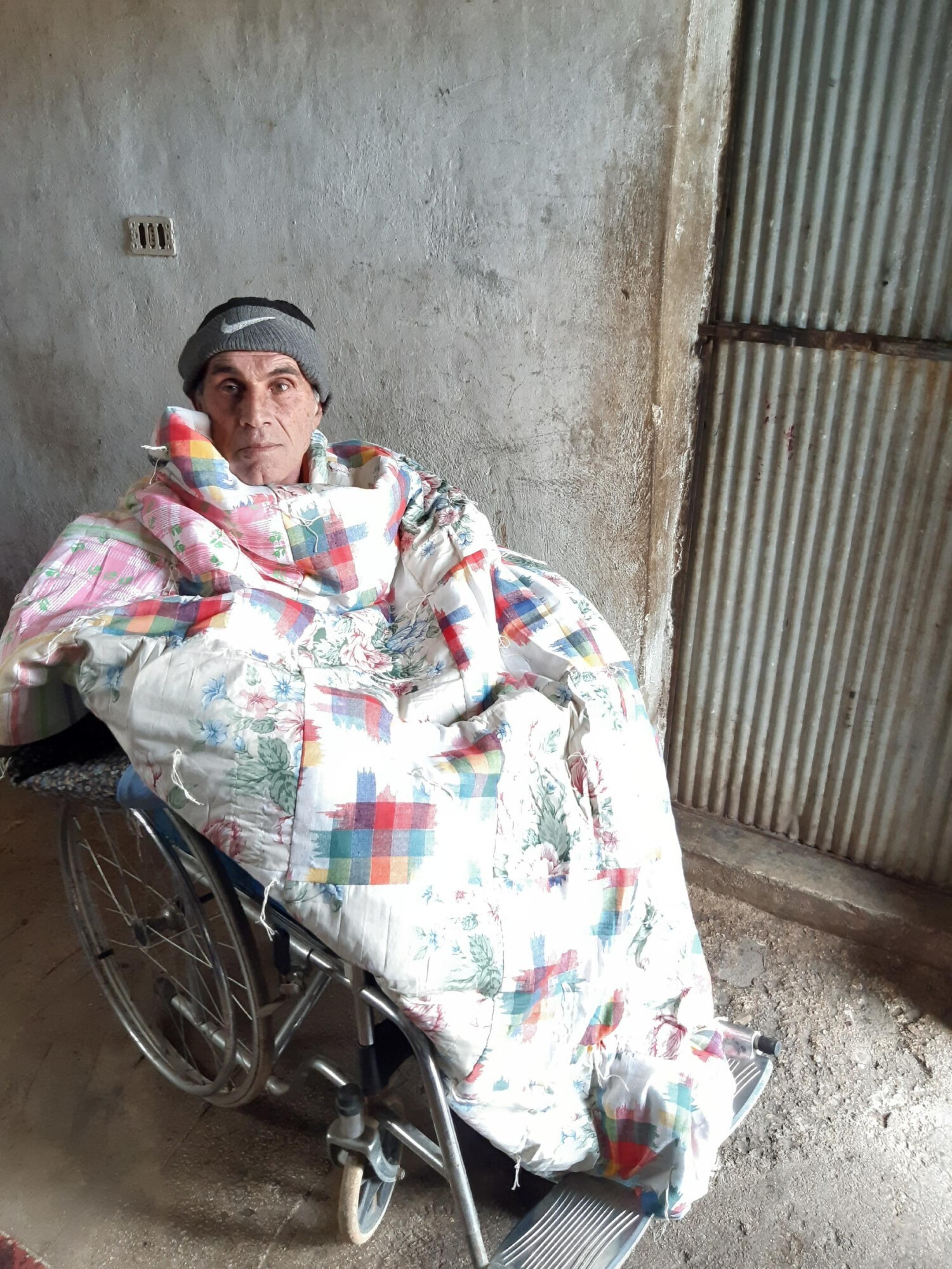 A man sitting in a wheelchair wrapped in a quilt