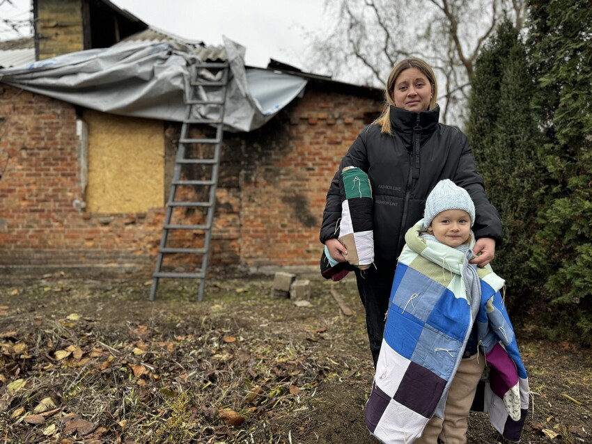 Yana stands near her house holding an MCC comforter in Nikopol, Ukraine, which was partially destroyed by shelling after the Russian military invasion of February 2022.